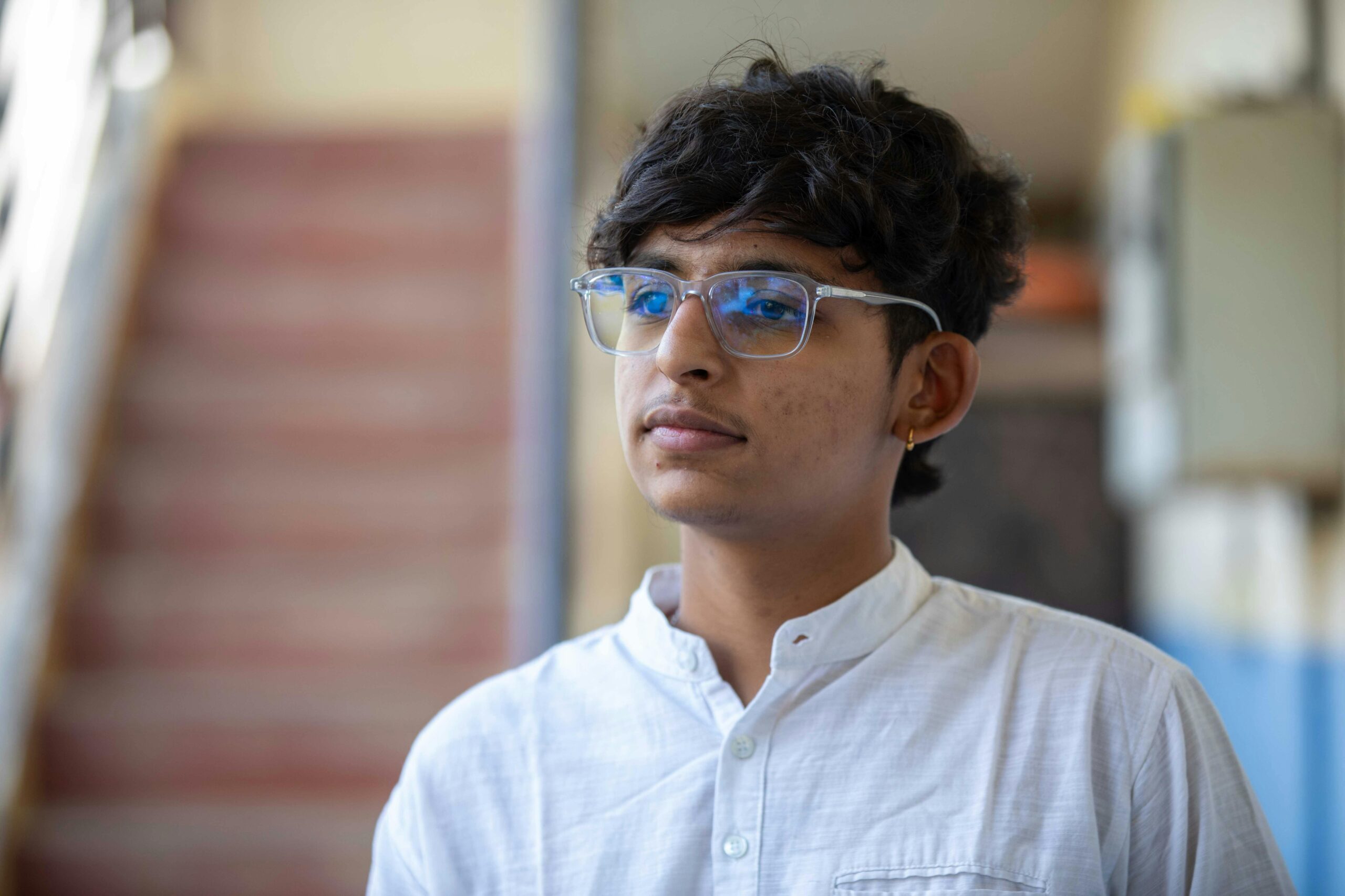 Portrait of a young man wearing glasses and a white shirt, looking thoughtfully indoors.