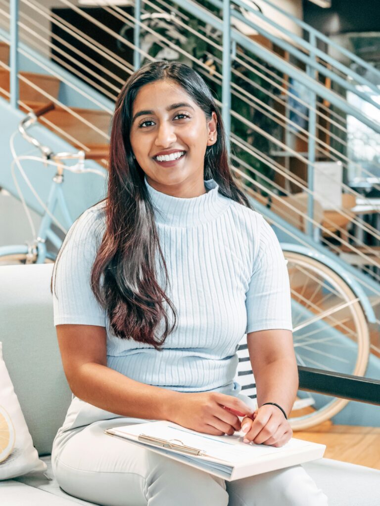 A smiling woman sitting indoors, exuding warmth and confidence.